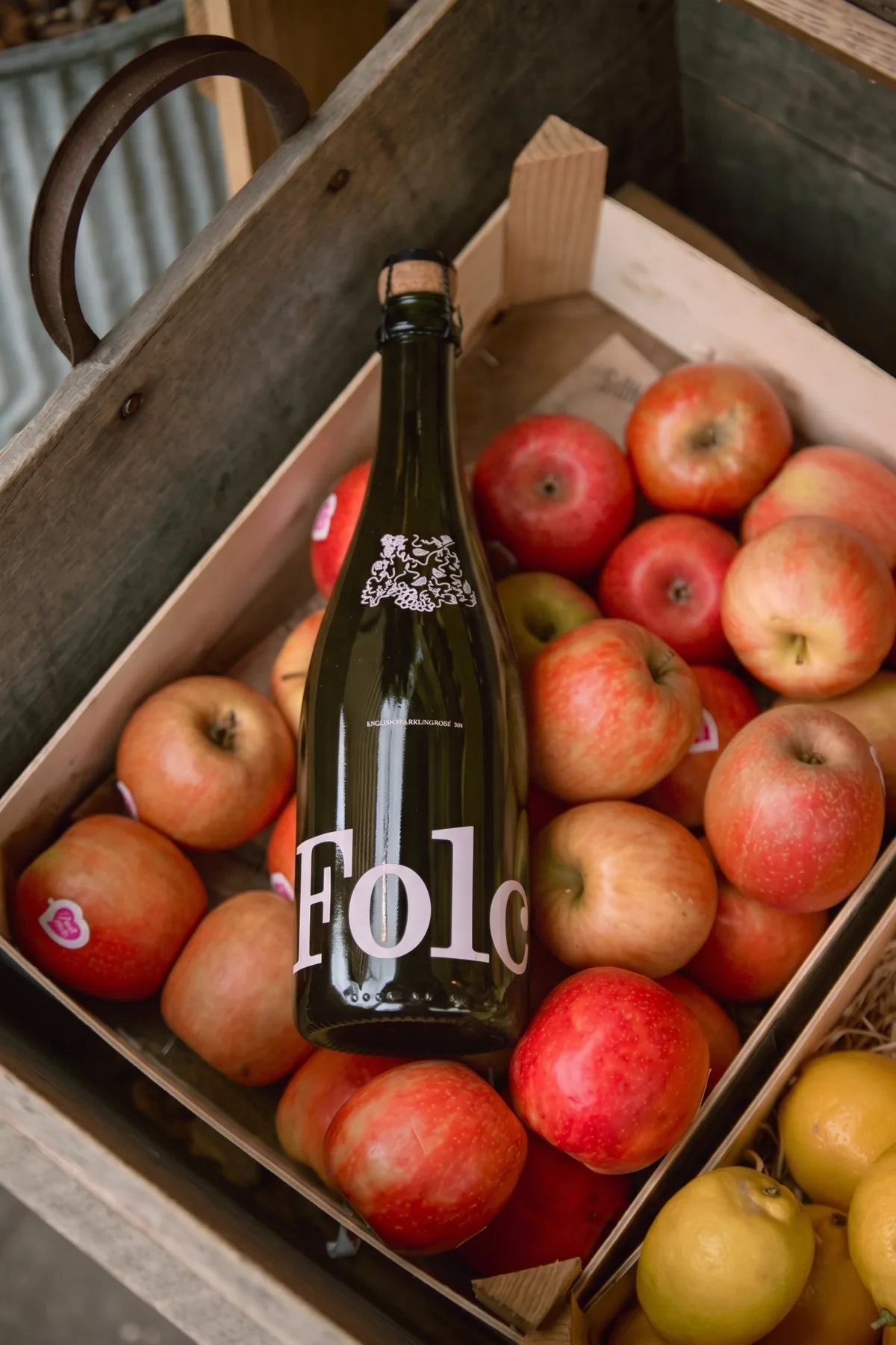 A bottle of Folc lying in a crate of red apples