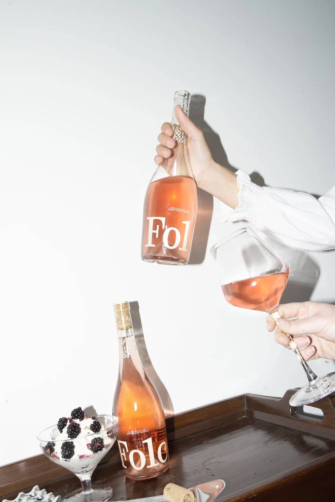 A bottle of Folc rosé poured into a glass beside a bowl of berries