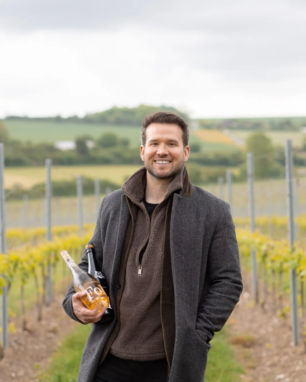 Tom, Folc's founder, in a vineyard holding two bottles of Folc