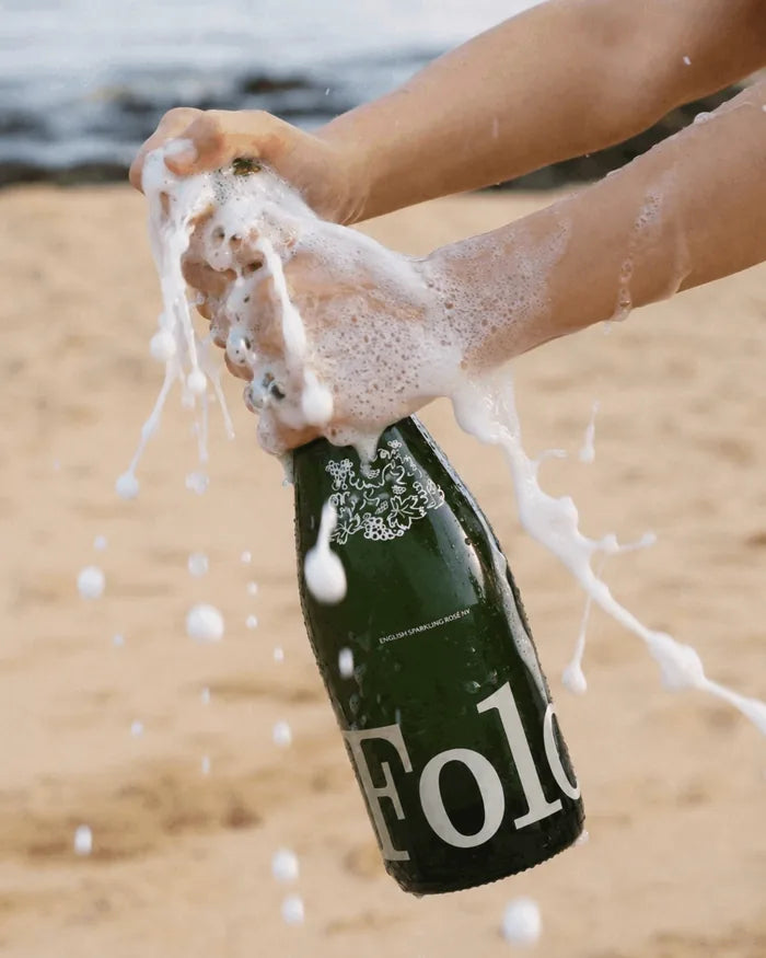 A bottle of Folc sparkling rosé foaming over on the beach