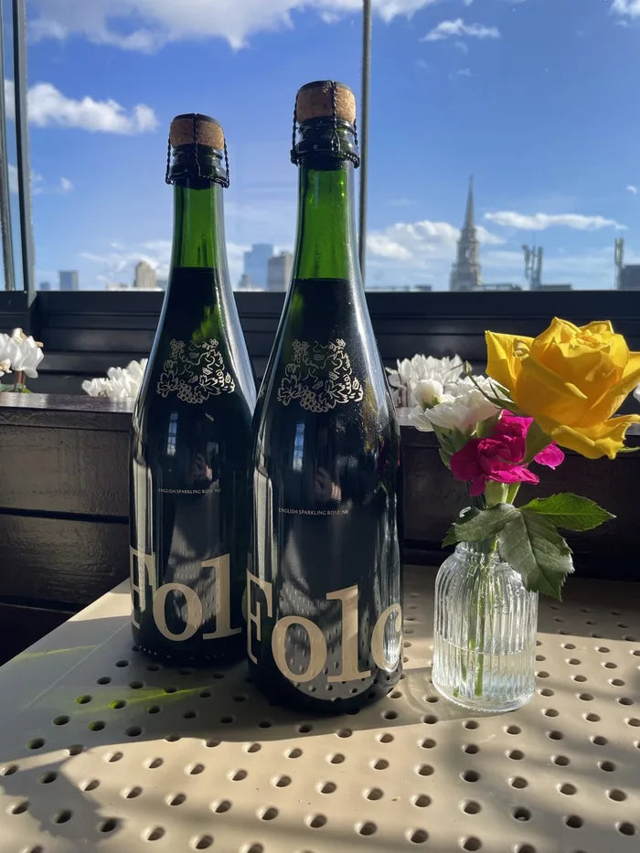 Two bottles of Folc sparkling rosé on a sunny rooftop with flowers