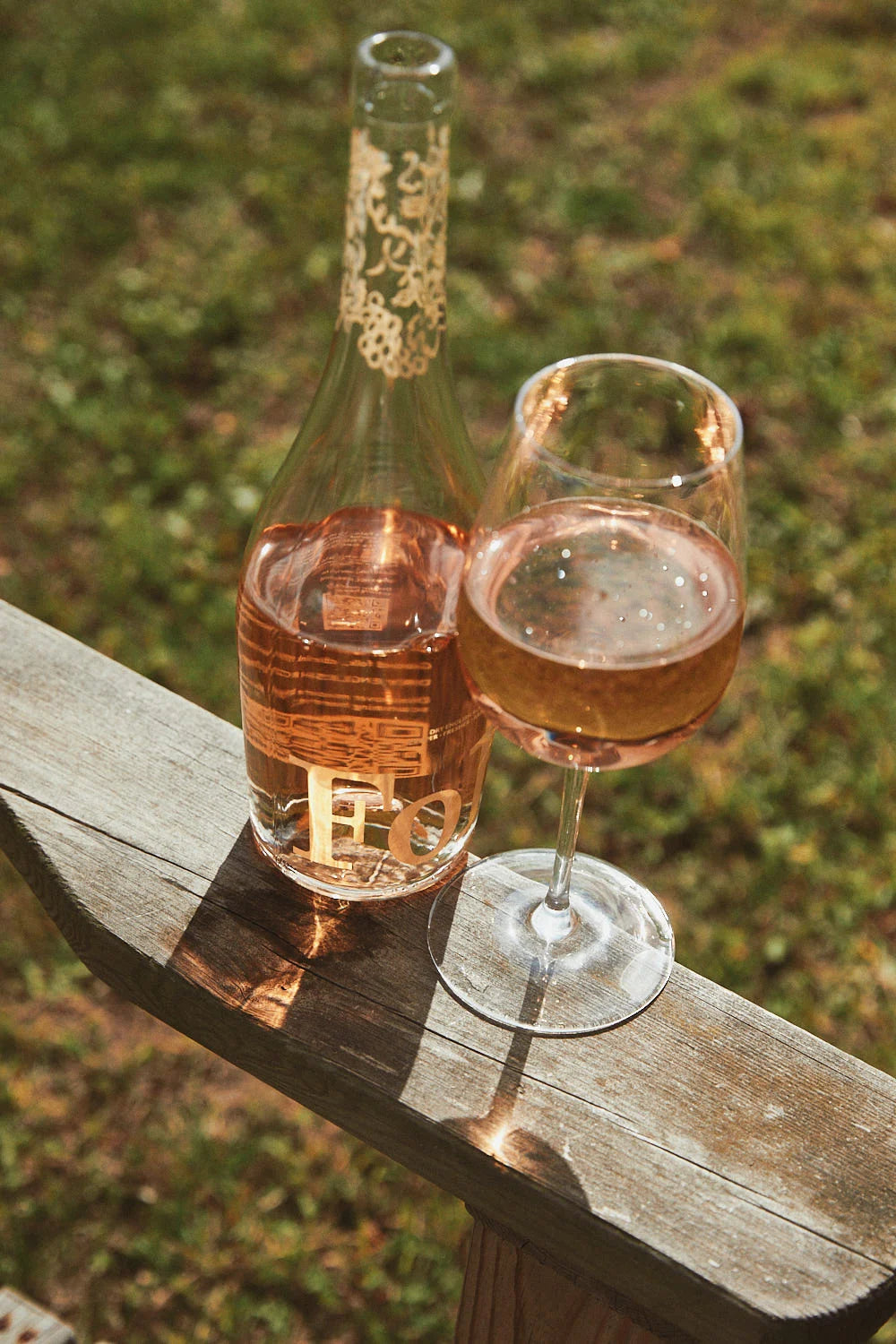 A bottle and glass of Folc rosé on a sunny bench